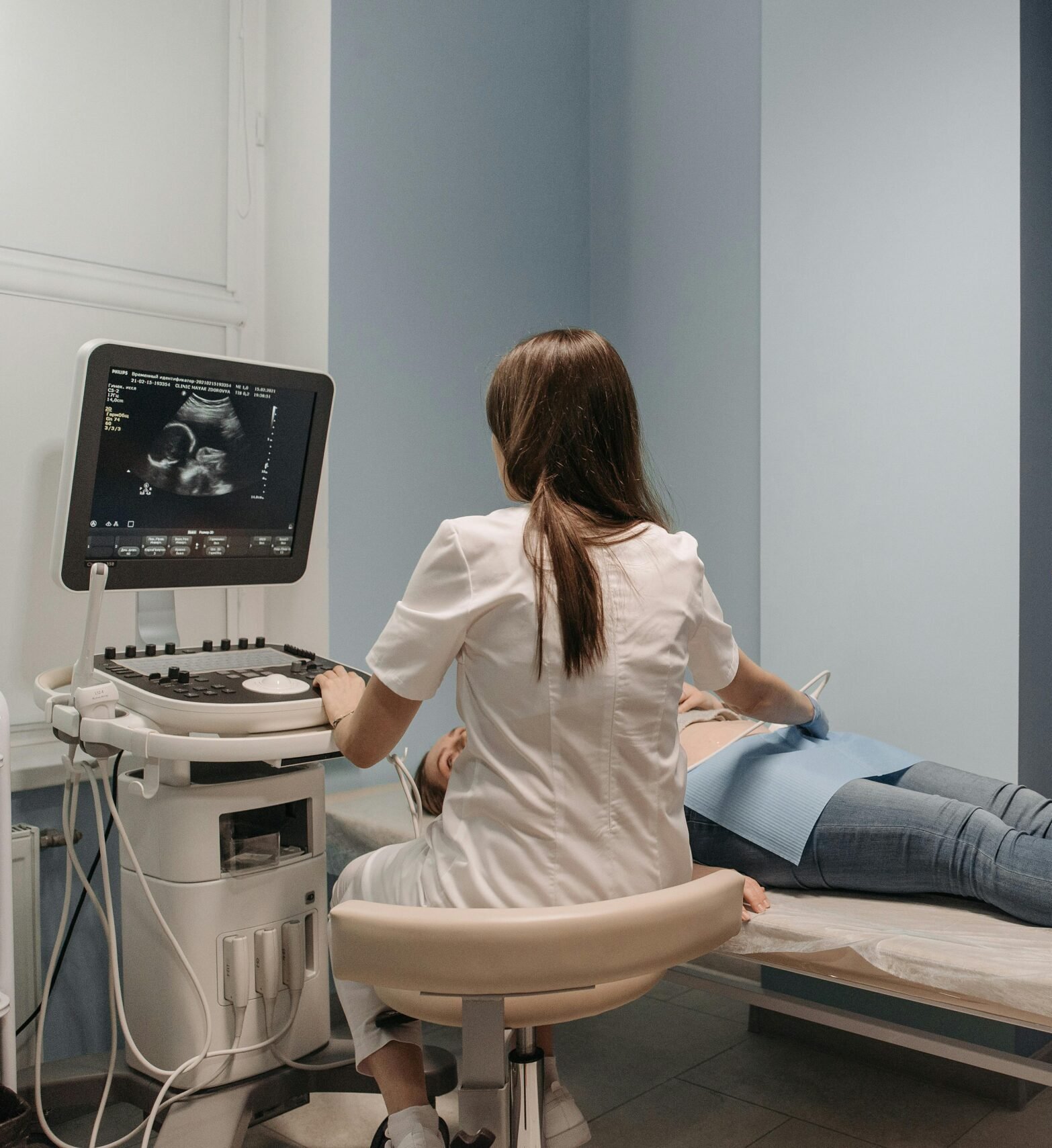 A doctor performs an ultrasound on a pregnant woman, while a man takes a photo in a clinical environment.
